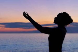 Woman holding hands in the air with sunset behind for solfeggio healing frequencies